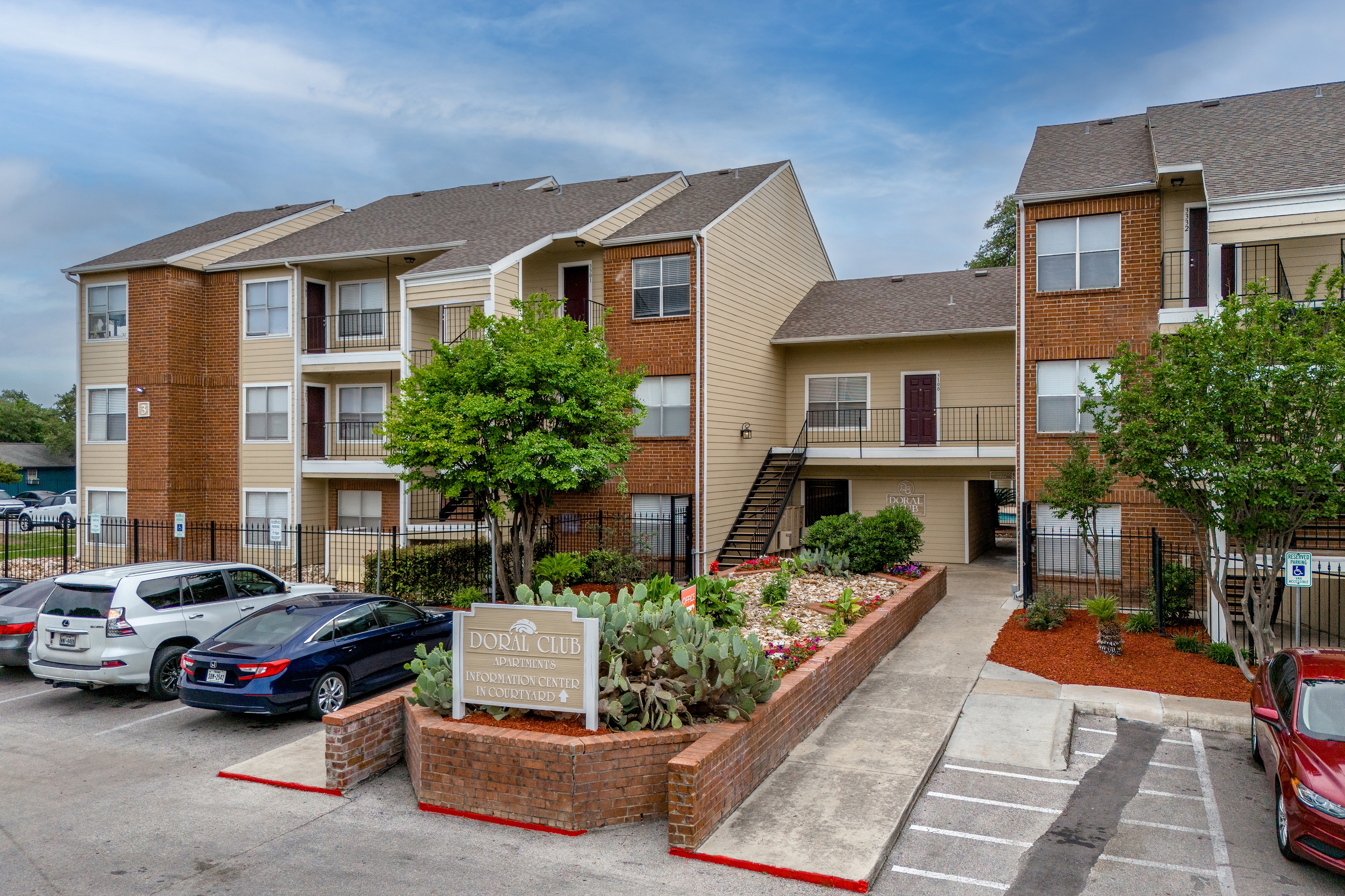 A parking lot in front of a brick apartment building with a sign that says 